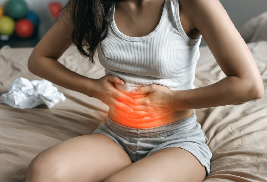 Young Woman Seated On Bed Experiencing Abdominal Pain.png